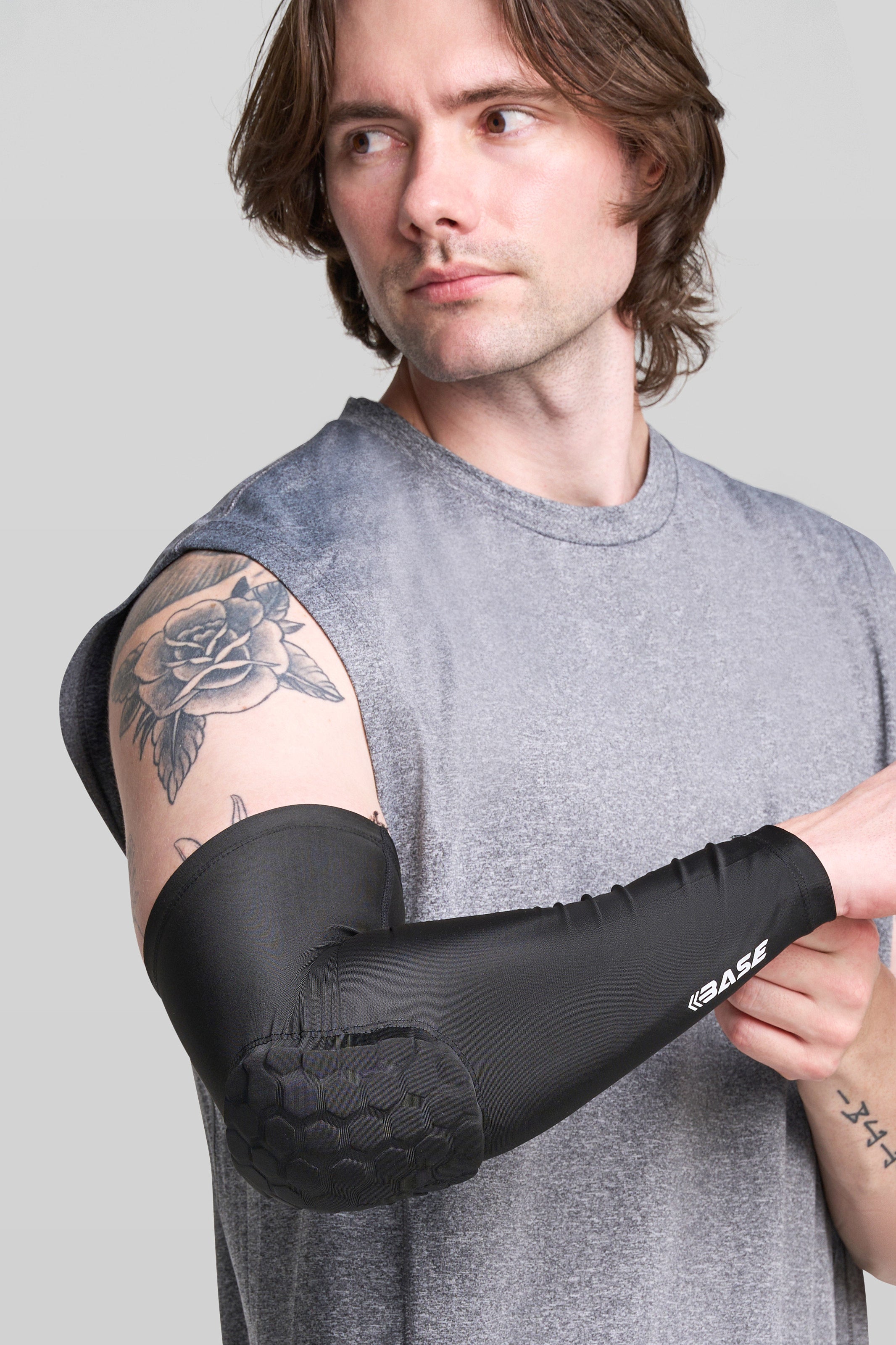 Person wearing a black elbow brace with 'BASE' branding on a gray background