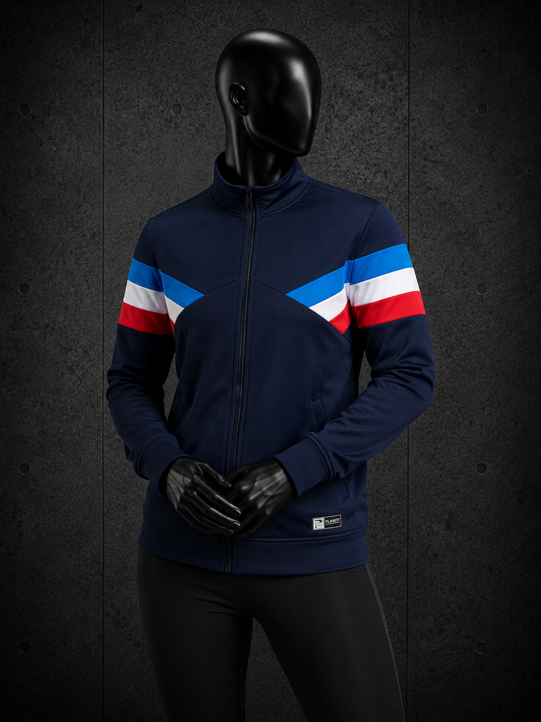 A mannequin wearing a navy blue zip-up jacket with bold diagonal red, white, and blue stripes across the shoulders and upper arms, paired with black gloves and black pants, set against a dark textured studio background.