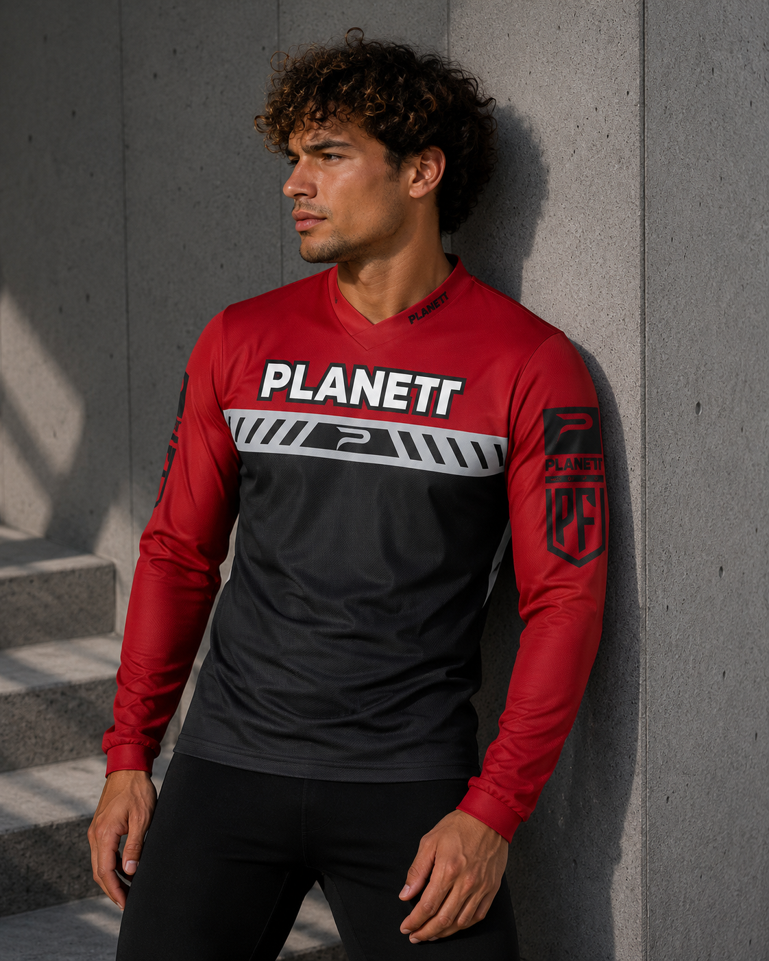 Man wearing a red and black sports jersey with 'PLANETI' logo against a gray wall.