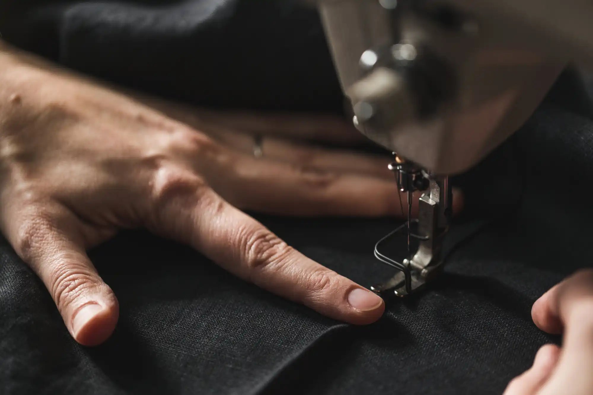 A sewing machine needle and presser foot with fabric being guided by human hands.