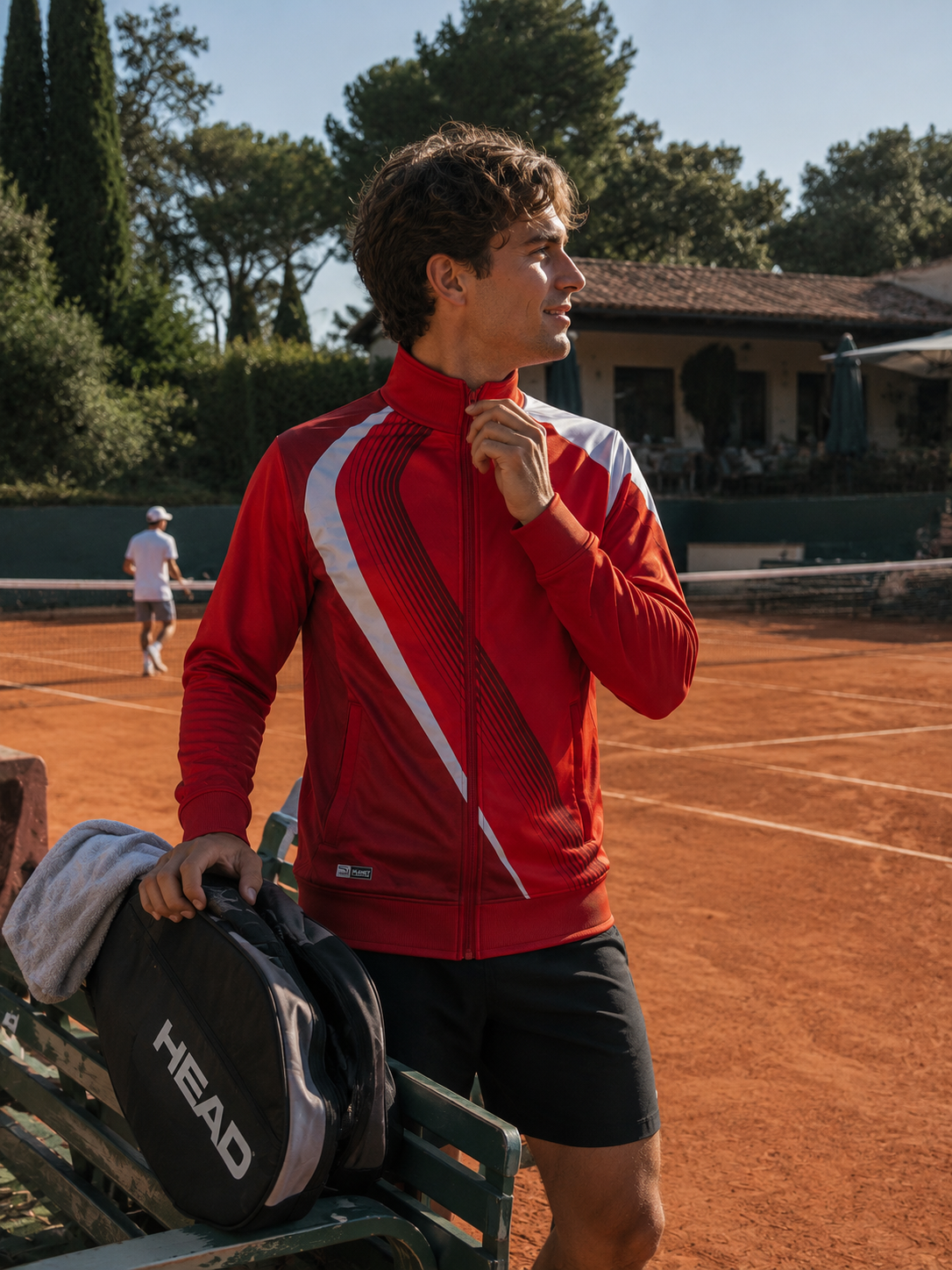Person in a red jacket on a tennis court with another person in the background.