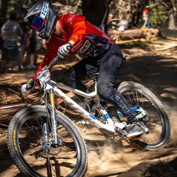 A mountain biker in full gear on a white full-suspension bike, kicking up dust on a dirt trail.