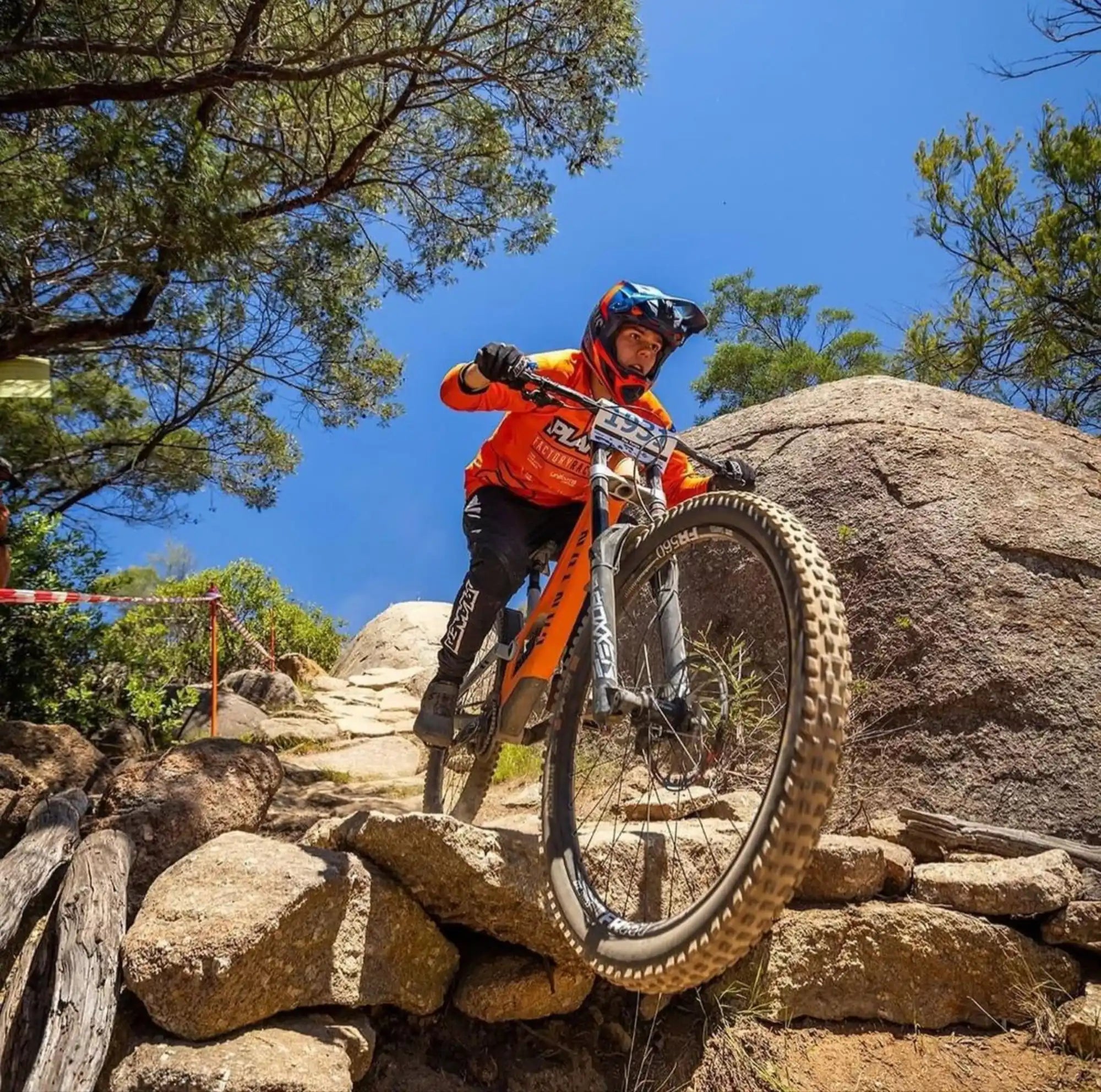 A mountain biker in full protective gear descending a rocky trail.