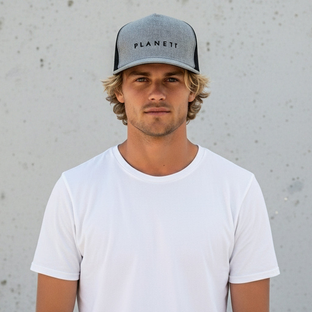 A man with blond, curly hair wearing a white t-shirt and a grey and black trucker hat.