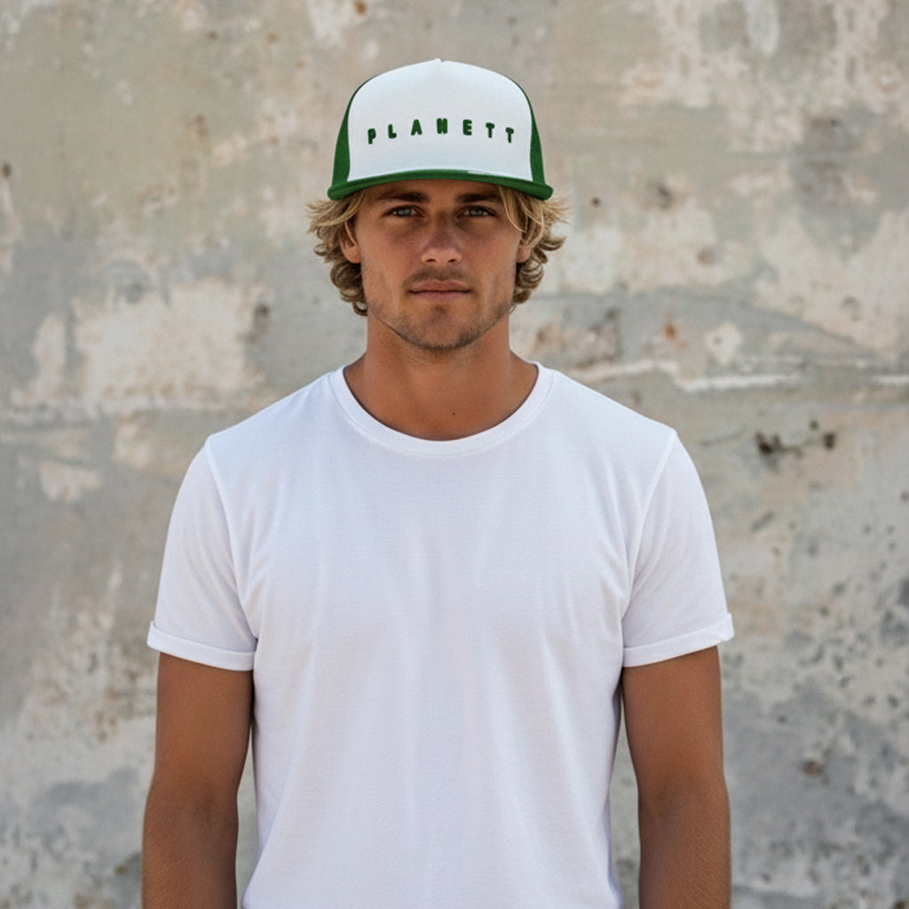 A man wearing a white t-shirt and a white and green trucker hat.