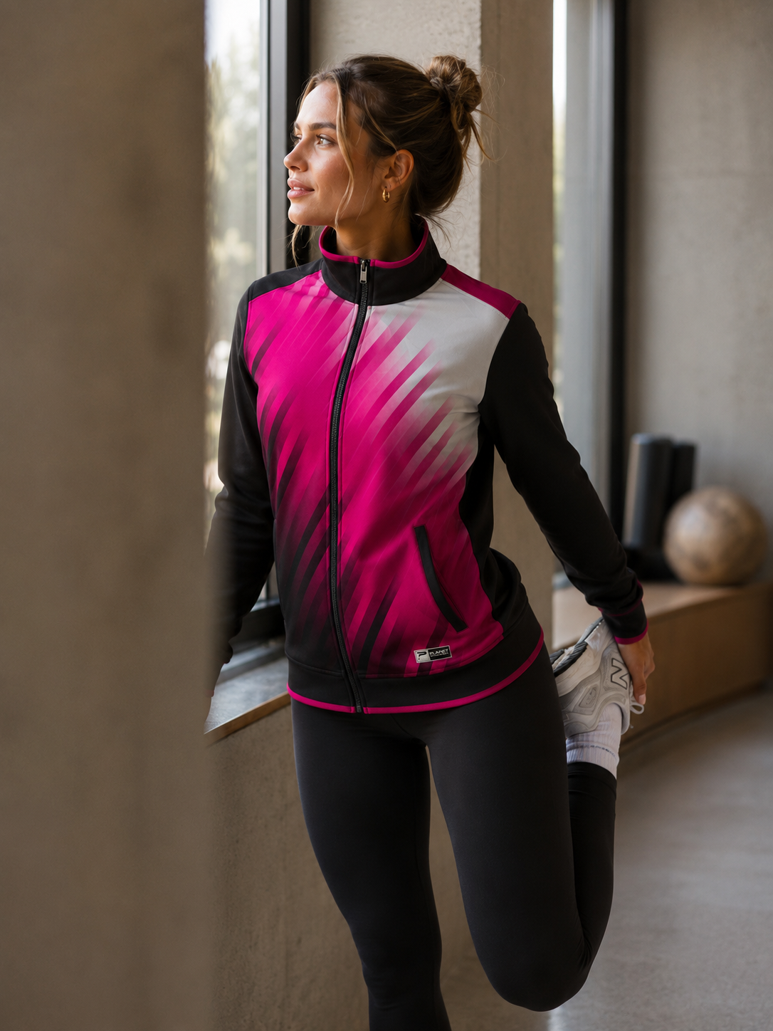 Woman in a pink and black athletic jacket stretching indoors.