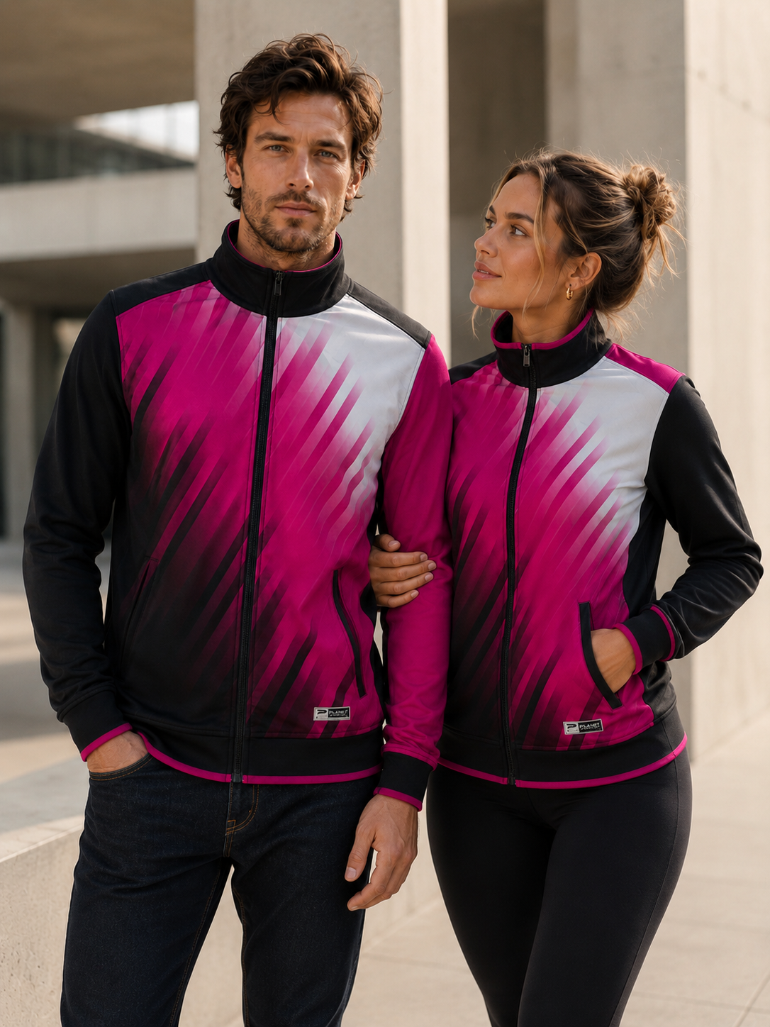 Two people wearing matching pink and black jackets in an urban setting.