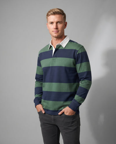 A man wearing a long-sleeve rugby shirt with horizontal navy blue and sage green stripes, paired with a white collar and dark gray pants, standing against a neutral gray studio background.