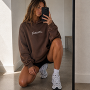 Person wearing a brown 'planett.' hoodie taking a mirror selfie.