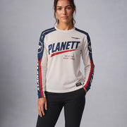 A woman modeling a long-sleeve athletic jersey with 'PLANETT' printed across the chest in navy and red, paired with black leggings, against a neutral gray studio background.