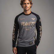 A man wearing a long-sleeve crew-neck athletic jersey with 'PLANETT MOTO CREW' printed on the front, featuring a gray body, black sleeves, and gold lettering, posed against a neutral gray studio background.