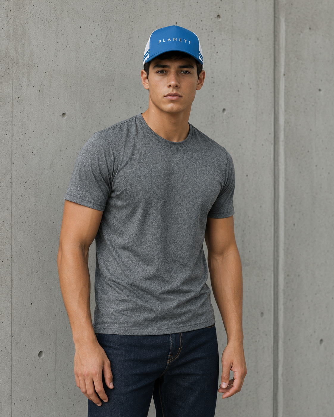 A man wearing a heather gray crewneck t-shirt and a blue baseball cap with 'PLANETS' printed on it, standing against a textured gray concrete wall.