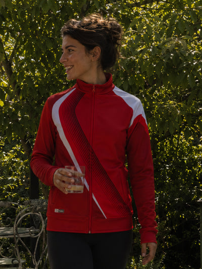 Woman wearing a red and white jacket standing outdoors with greenery in the background