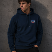 Man wearing a navy blue hoodie with a logo against a gray concrete wall