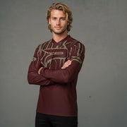 A man with wavy blonde hair, light stubble, and a maroon long-sleeved shirt with a geometric pattern on the shoulders and chest.