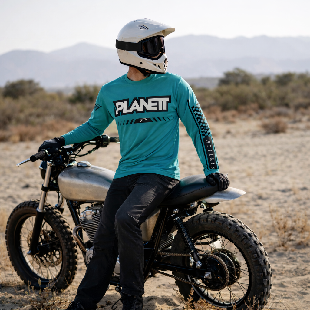A teal long-sleeved planet 2 motocross jersey with black and white graphics, worn by a rider in desert terrain.