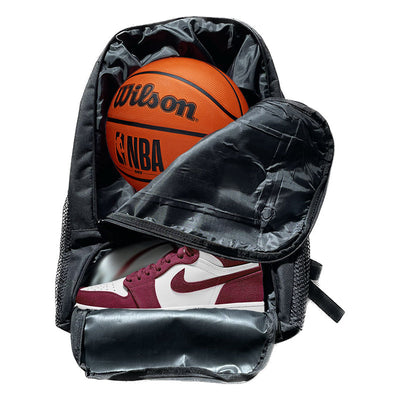 Black backpack with mesh side pockets and a zippered compartment containing an orange wilson nba basketball and maroon and white nike air jordan 1 sneaker.