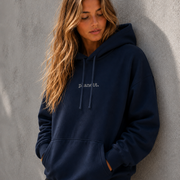 Woman wearing a navy hoodie with 'planet' logo against a gray wall