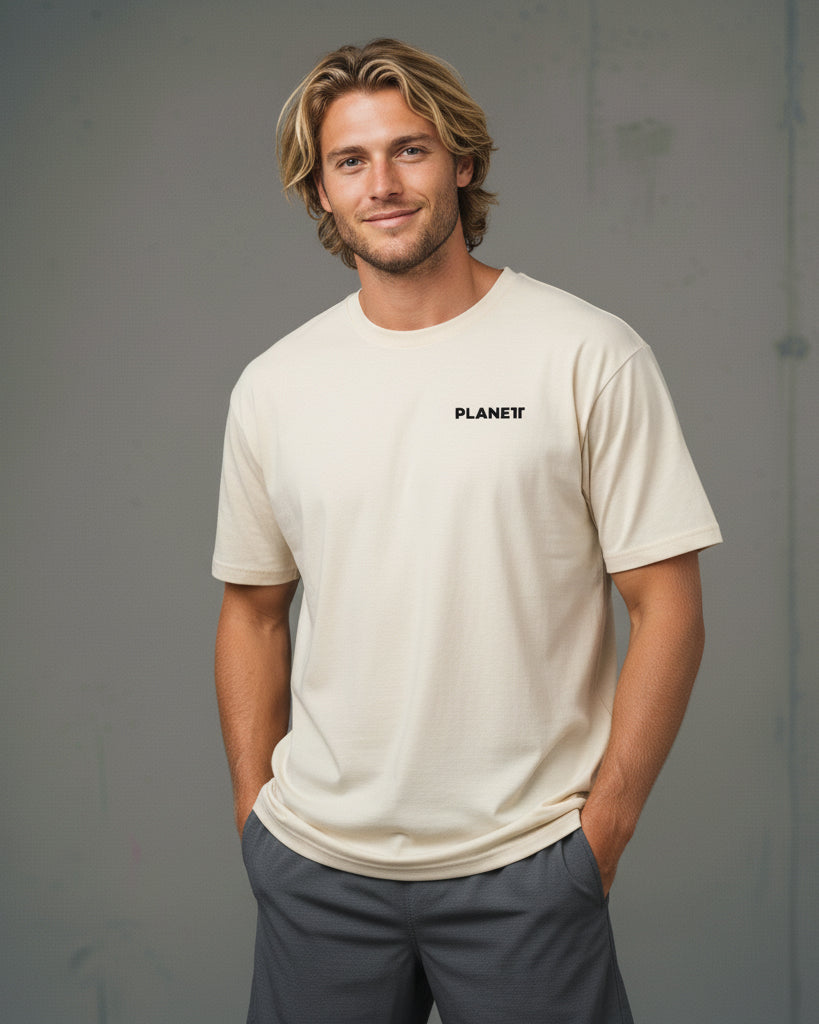 A smiling man wearing a light beige short-sleeve crewneck t-shirt and dark gray shorts.