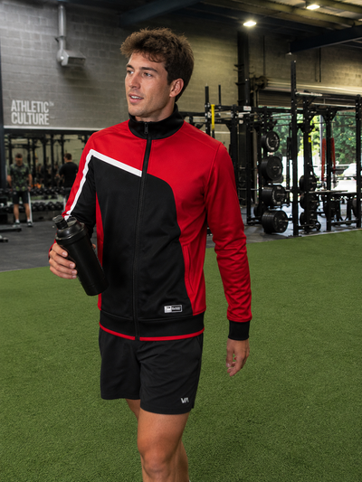 Man in a red and black athletic outfit holding a water bottle in a gym.