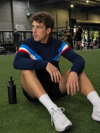 Person sitting on a gym floor with athletic wear and water bottle
