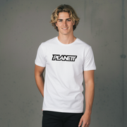 A smiling young man with shoulder-length blonde hair wearing a white crew-neck t-shirt with ’PLANETT’ in black outline lettering and black pants.
