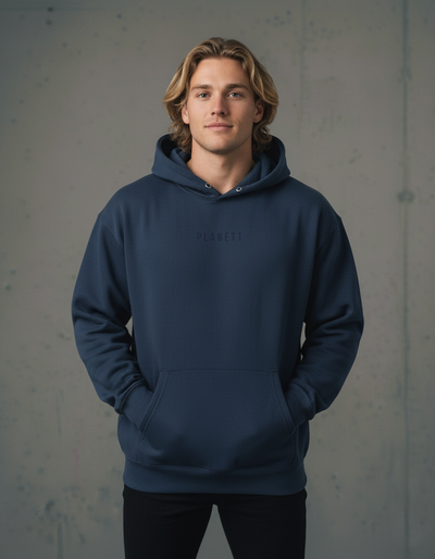 A young man models a plain navy blue hoodie with a small, subtly embossed logo on the chest and a front pouch pocket.