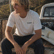 Man sitting on a truck bed wearing a white t-shirt with 'PLANET' logo.
