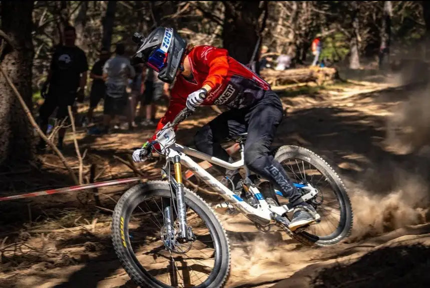 White mountain bike with gold suspension forks and black tires, ridden by a cyclist in red gear