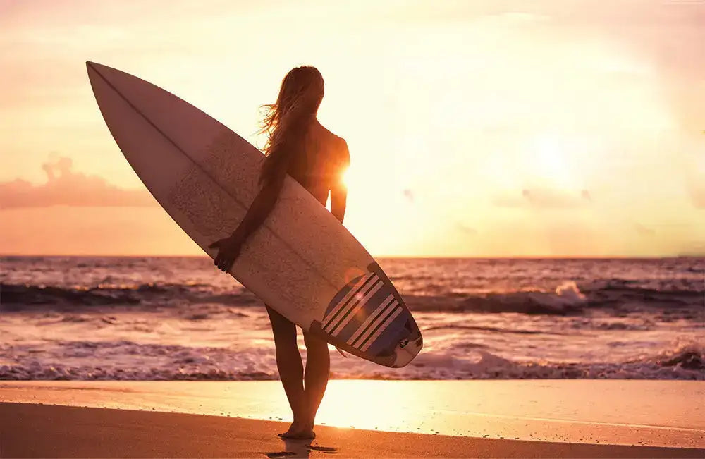 White surfboard with a blue and black striped design near the tail, held by a person at sunset.