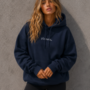 Woman wearing a navy blue hoodie with 'planet' logo against a gray wall