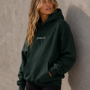 Woman wearing a dark green hoodie with 'plant it' text against a gray wall