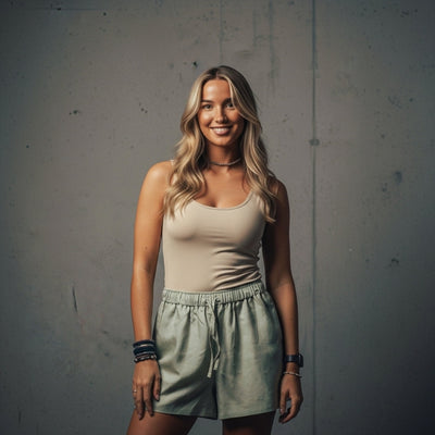 A young woman with long blonde hair, wearing a beige tank top and light green shorts.
