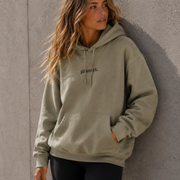 Woman wearing a green hoodie leaning against a gray wall