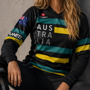 Woman wearing a sports jersey with 'Australia' text and Australian flag, sitting against a concrete wall.