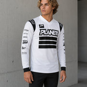 Person wearing a white long-sleeve shirt with black accents and branding, standing against a concrete wall.